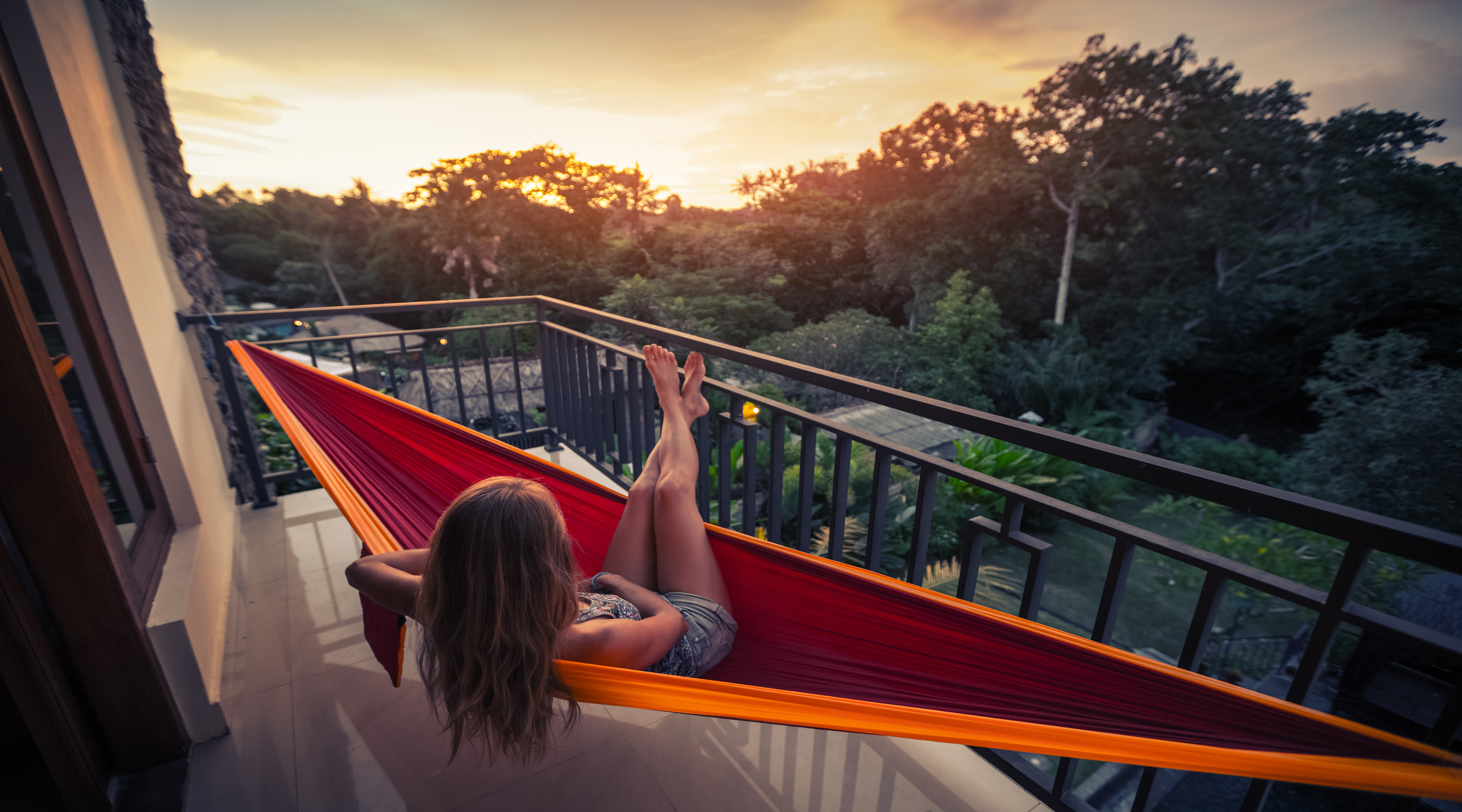 Young woman enjoys sunset relaxing in the hammock on the balcony 